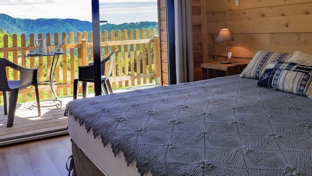 Un dormitorio con una cama grande, piso de madera, un balcón con mesa y sillas, y vistas a las montañas.