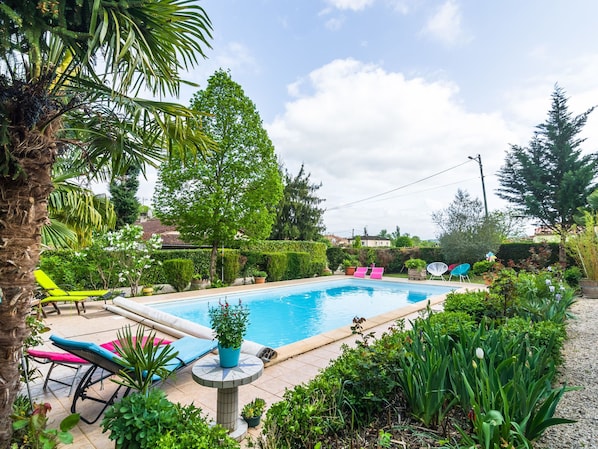 A swimming pool surrounded by lush greenery, with lounge chairs and potted plants.