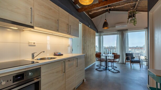 A modern kitchen with wooden cabinets, stainless steel appliances, and a dining area with a view of the city.