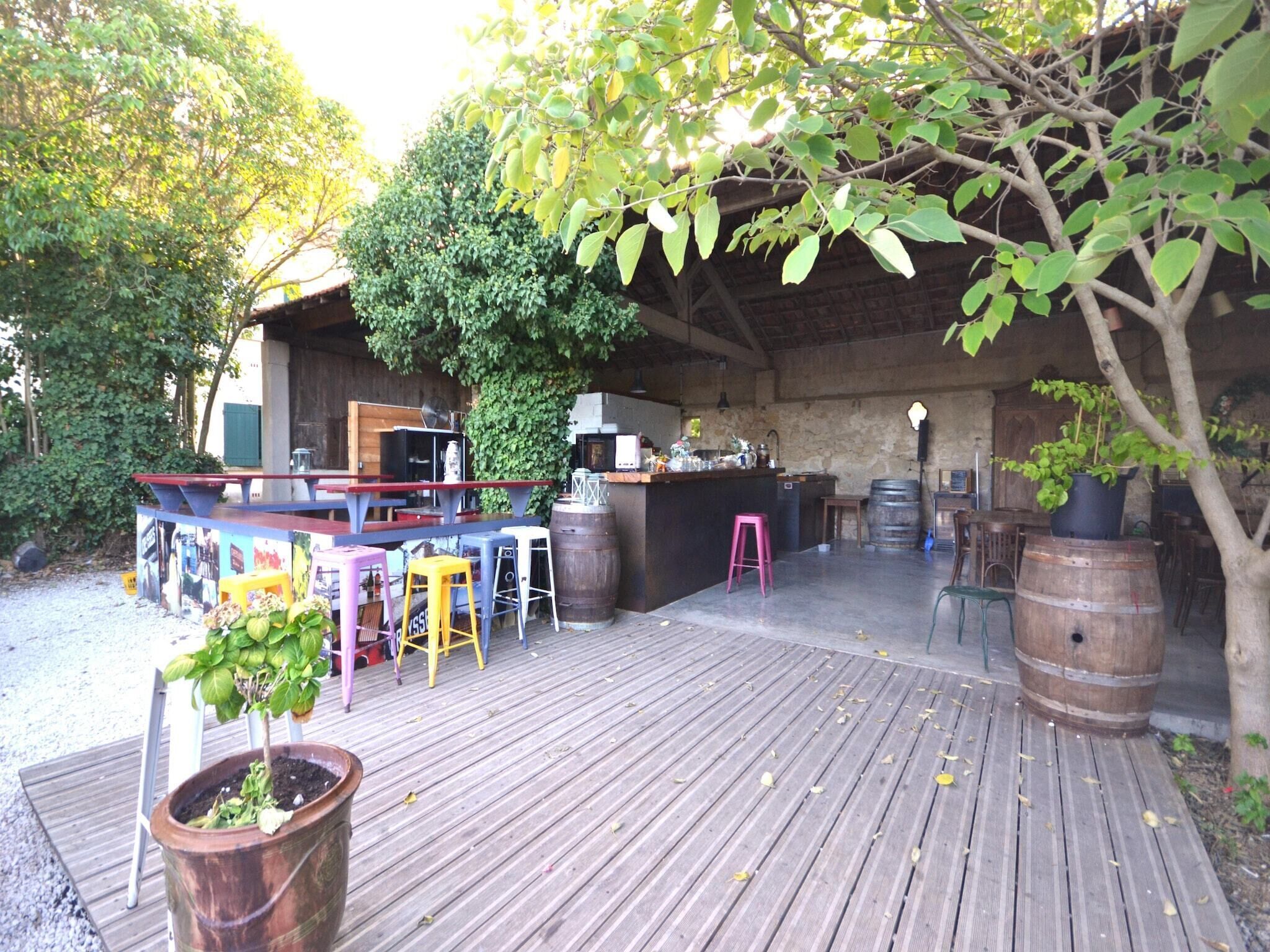 Un espace de restauration en plein air avec des tables et des chaises en bois, un comptoir de bar et, en arrière-plan, un mur de pierres rustiques.