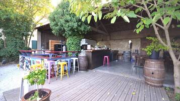 Un espace de restauration en plein air avec des tables et des chaises en bois, un comptoir de bar et, en arrière-plan, un mur de pierres rustiques.
