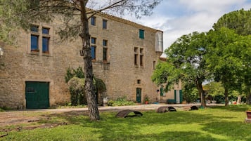 Un bâtiment en pierre avec une porte et des fenêtres vertes, entouré d’herbe et d’arbres.