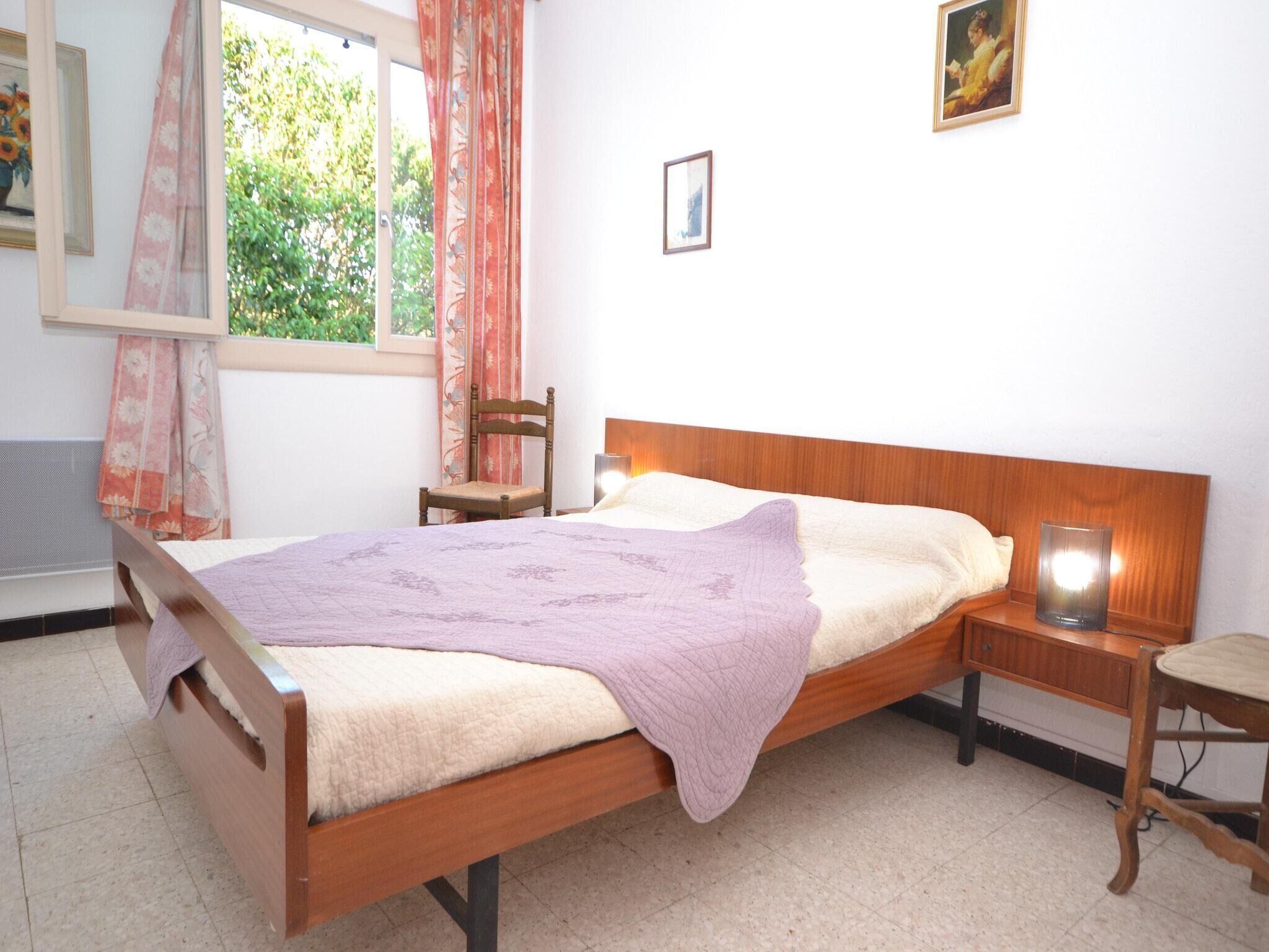 A bedroom with a wooden bed, a nightstand, a chair, a window with curtains, and a painting on the wall.