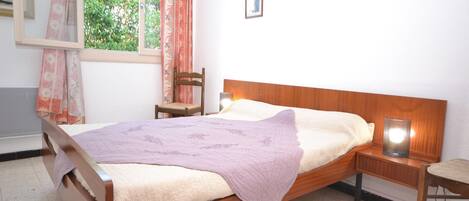 A bedroom with a wooden bed, a nightstand, a chair, a window with curtains, and a painting on the wall.