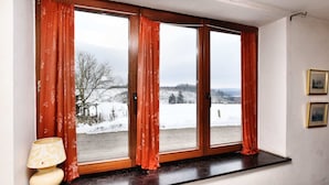 A room with a large window, a wooden window sill, and a wall-mounted lamp.