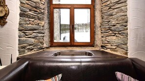 A stone-walled room with a large window and a massage table.