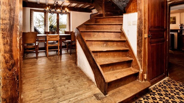 A rustic wooden staircase leading to a lofted area with exposed beams and stone walls.