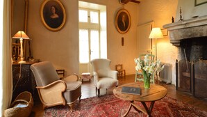 Quarto tradicional com lareira, duas poltronas, uma mesa de centro redonda e um tapete estampado.