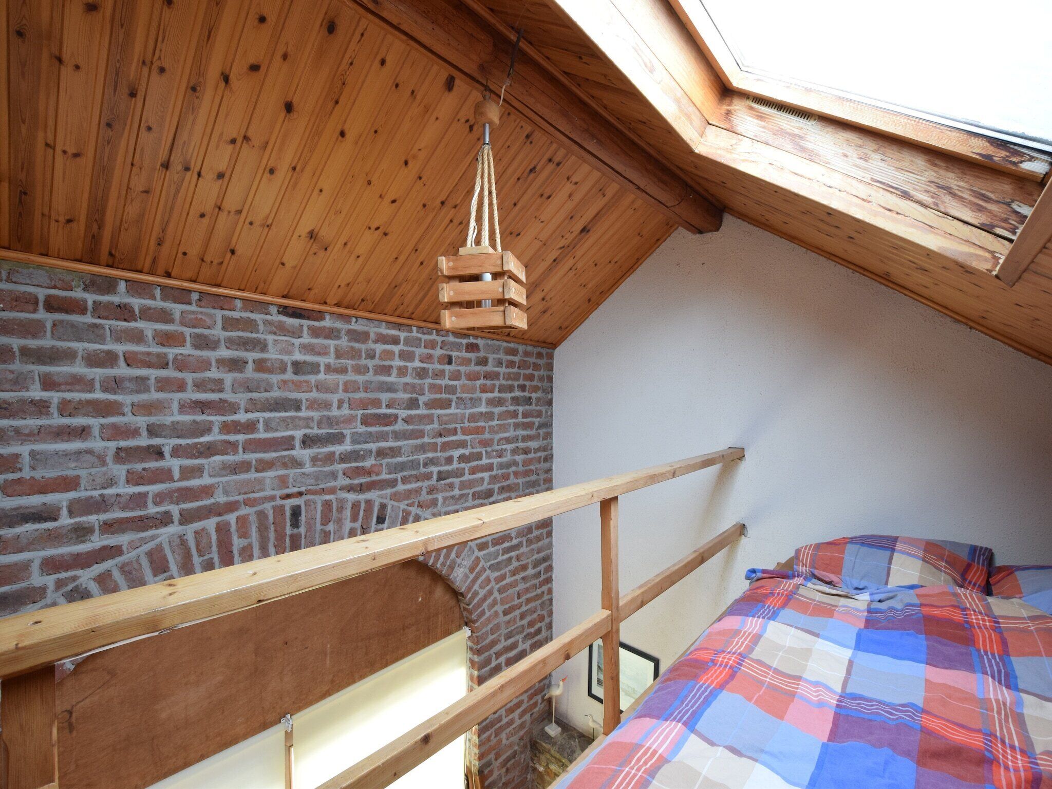 Un dormitorio tipo loft con techo de madera, paredes de ladrillo visto y tragaluces.