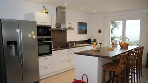 Une cuisine moderne équipée d’un four encastré, d’un micro-ondes et d’un réfrigérateur. On y trouve également un grand îlot central avec des tabourets de bar et une fenêtre donnant sur l’extérieur.