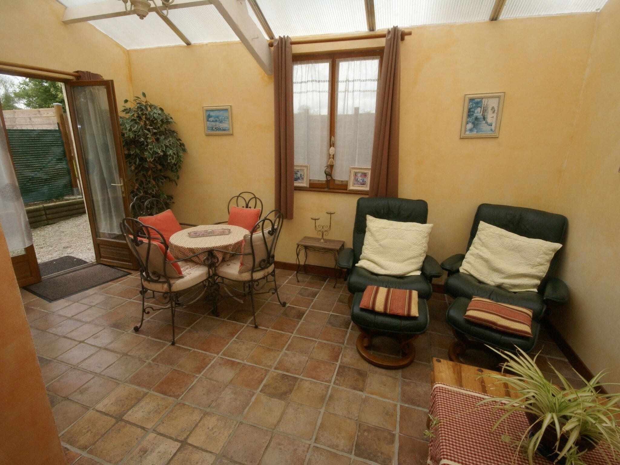 A sunroom with a tiled floor, a table with chairs, two armchairs, a small table with a candle, and a potted plant.