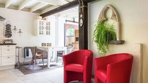 A modern kitchen with white cabinets, a dining area with wicker chairs, and a red chair in the foreground. - Charming Retreat, Veldegem (Zedelgem - Veldegem)