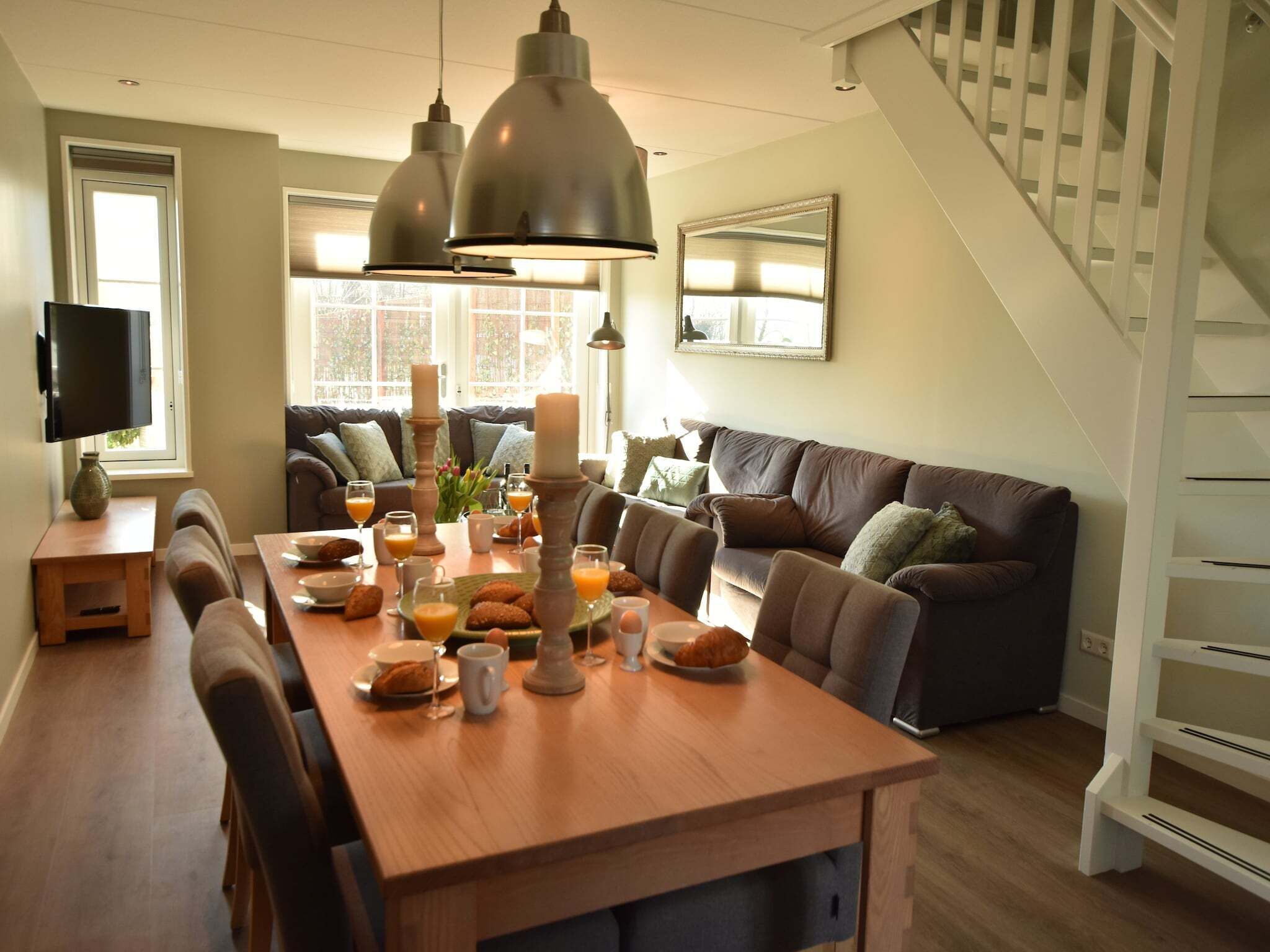 Een eetgedeelte met een houten tafel gedekt voor het ontbijt, een bank en een trap.