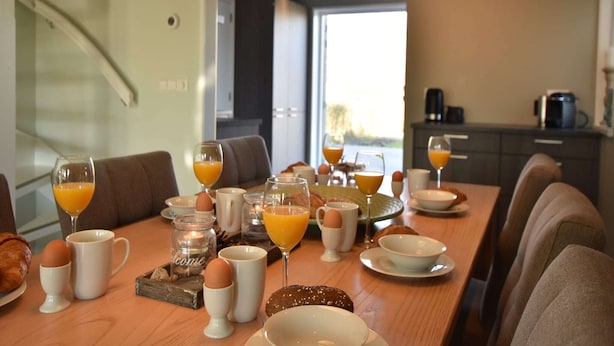 Une table mise pour le petit-déjeuner, avec une place pour deux personnes, comprenant des œufs, du pain et du jus d’orange.
