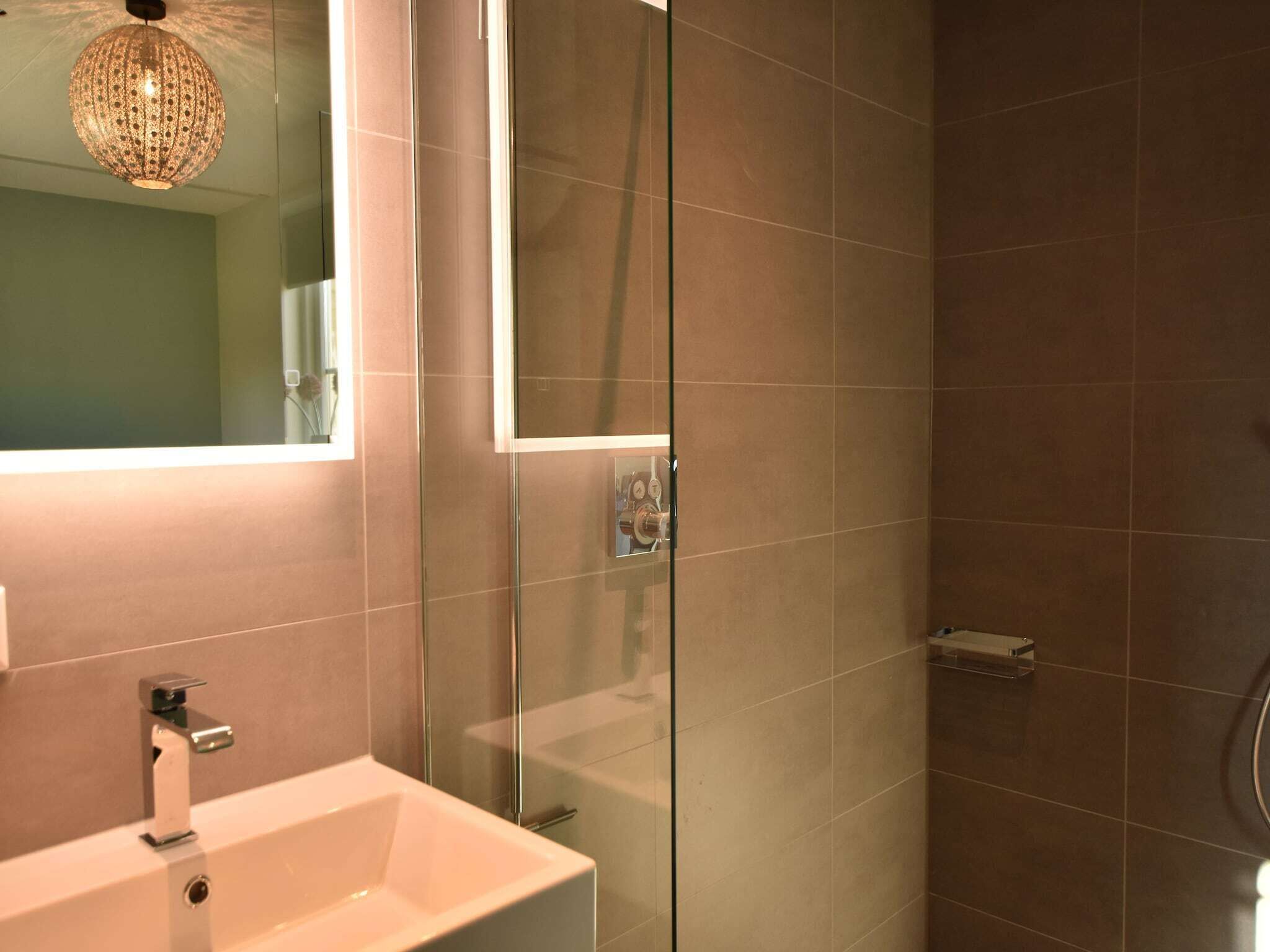 Ein modernes Badezimmer mit Duschkabine aus Glas, einem weißen Waschbecken und einem Spiegel.