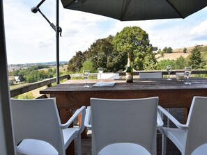 Een houten tafel met een fles en glazen, omringd door witte stoelen, met uitzicht op een schilderachtig landschap.