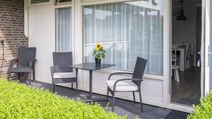 An outdoor patio with a table and two chairs, a potted plant, and a view of the interior through a glass door. - Apartment in Zoutelande near Sandy Beach (Zoutelande)