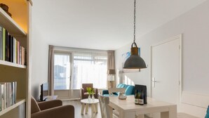 A modern living room with a sofa, a dining table, and a bookshelf. - Apartment in Zoutelande near Sandy Beach (Zoutelande)