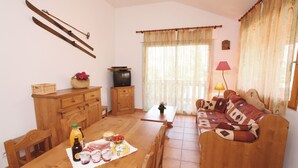 Una sala de estar acogedora con un sofá de madera, una mesa de comedor dispuesta con comida, un televisor y esquíes colgados en la pared.