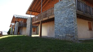 Un edificio de dos plantas con fachada de piedra, balcones de madera y un espacio exterior cubierto.