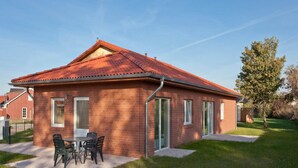 A single-story brick house with a red-tiled roof, a patio with a table and chairs, and a small garden area. - Charming Coastal Retreat in Zierow (Zierow)