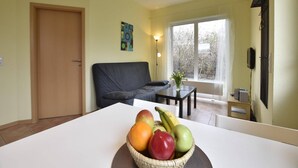 A living room with a sofa, a dining table with a fruit bowl, a window with a view of trees, and a door. - Charming Coastal Retreat in Zierow (Zierow)