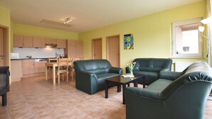 Een woonkamer met twee groene leren banken, een salontafel en een eethoek met een houten tafel en stoelen.
