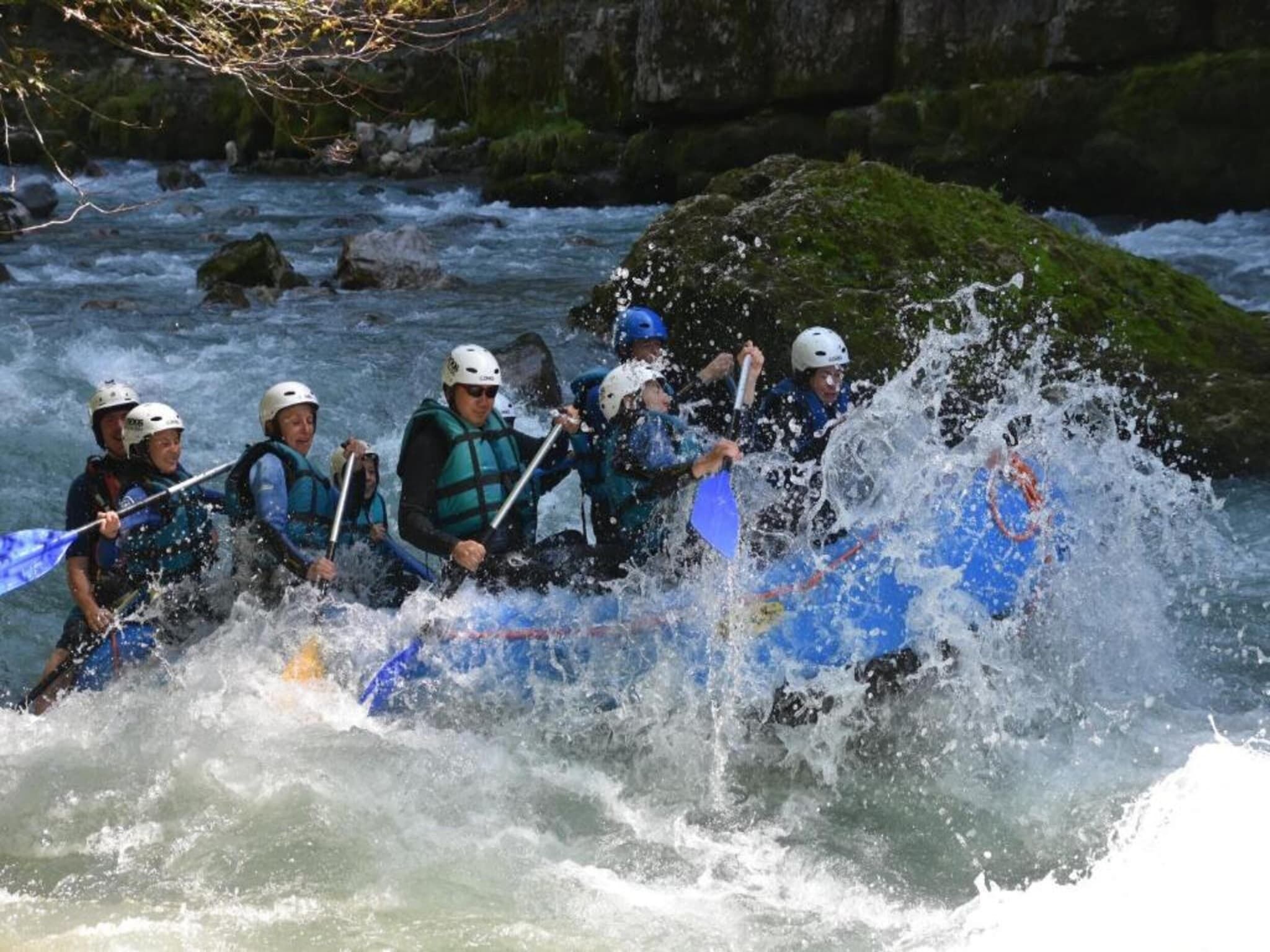 Un groupe de personnes à bord d’un radeau bleu navigue sur une rivière aux eaux tumultueuses.