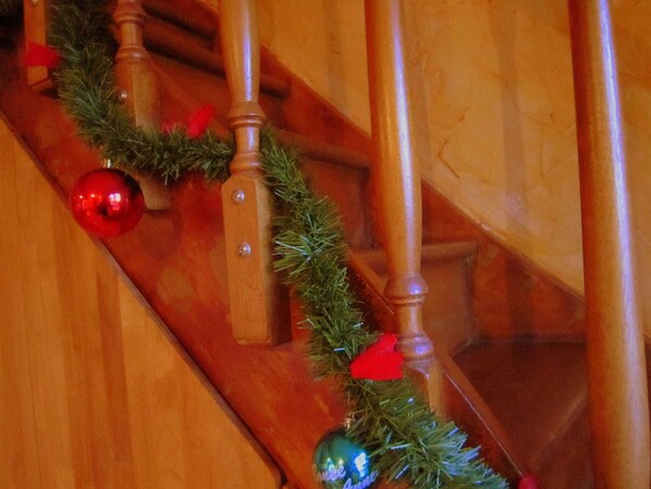 Una escalera de madera adornada con una guirnalda de follaje verde y adornos rojos.