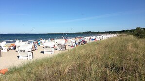 Ein Strand mit Liegestühlen und Sonnenschirmen, ein sandiger Uferstreifen und ein klarer, blauer Himmel.