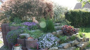 Ein Garten mit Steinpflanzgefäßen, einem Metallkübel und verschiedenen Blumen und Pflanzen.