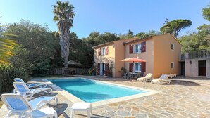 A pool area with lounge chairs and a building with a tiled roof.