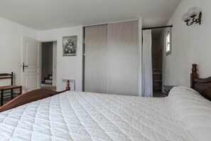 A bedroom with a bed, a chair, a wardrobe, and a bathroom visible through an open door.