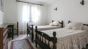A bedroom with two beds, a desk, a chair, and a window with curtains.