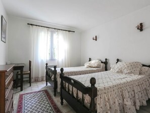 Quarto com duas camas, uma escrivaninha, uma cadeira e uma janela com cortinas.