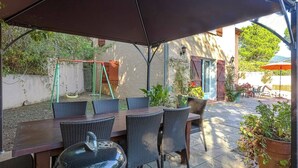 An outdoor patio with a covered dining area, a grill, and a swing set.