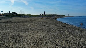 Een strand met een vuurtoren, boten en enkele mensen.