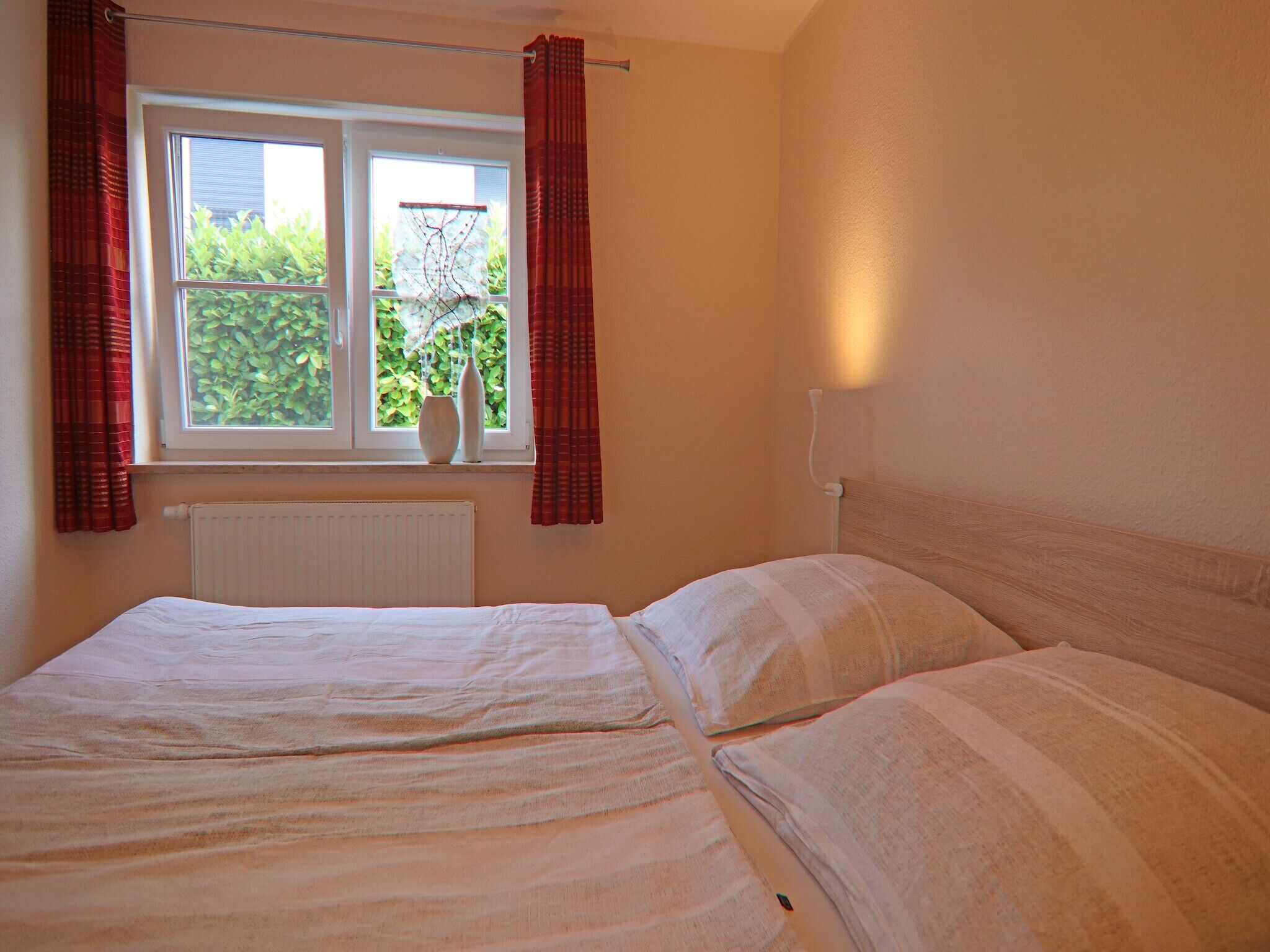 Quarto com cama, janela com cortinas, radiador e luminária na parede.