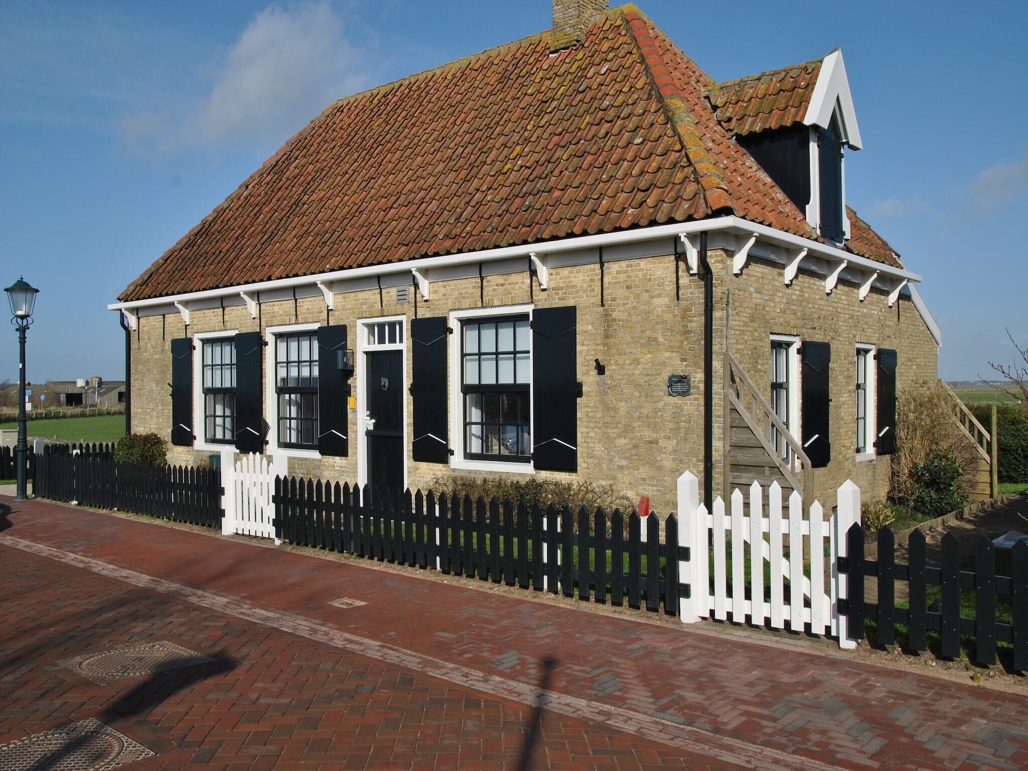 A traditional brick building with a tiled roof, white picket fence, and a small staircase leading to the entrance.