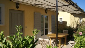 En terrasse med et bord og stole, et overdækket område med tag, og en dør.