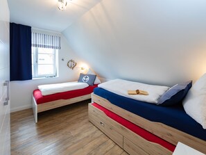 Une chambre avec deux lits, une fenêtre avec des rideaux, un luminaire fixé au mur et un plancher en bois.