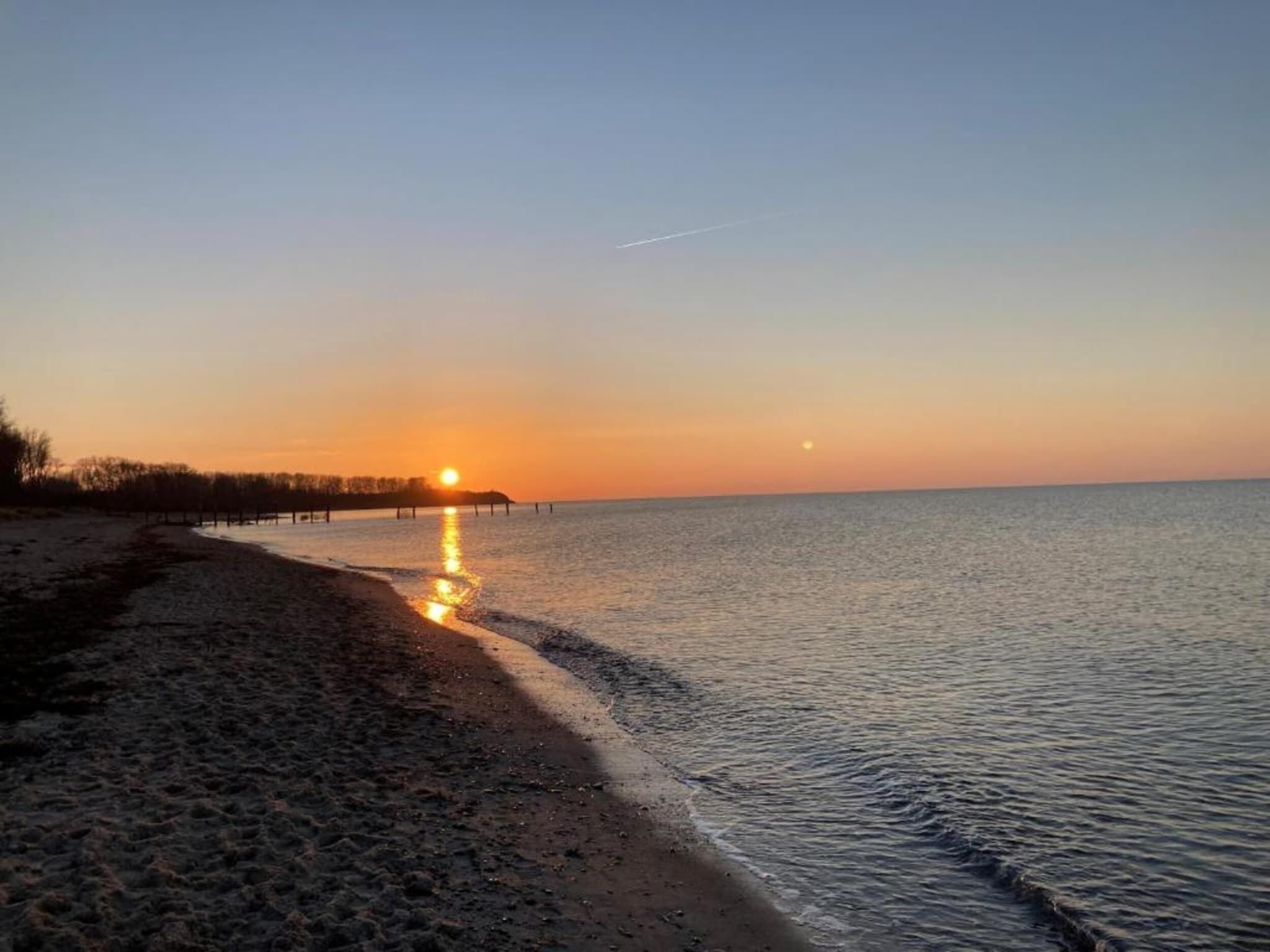 A beach with a sunset, calm water, and a clear sky.