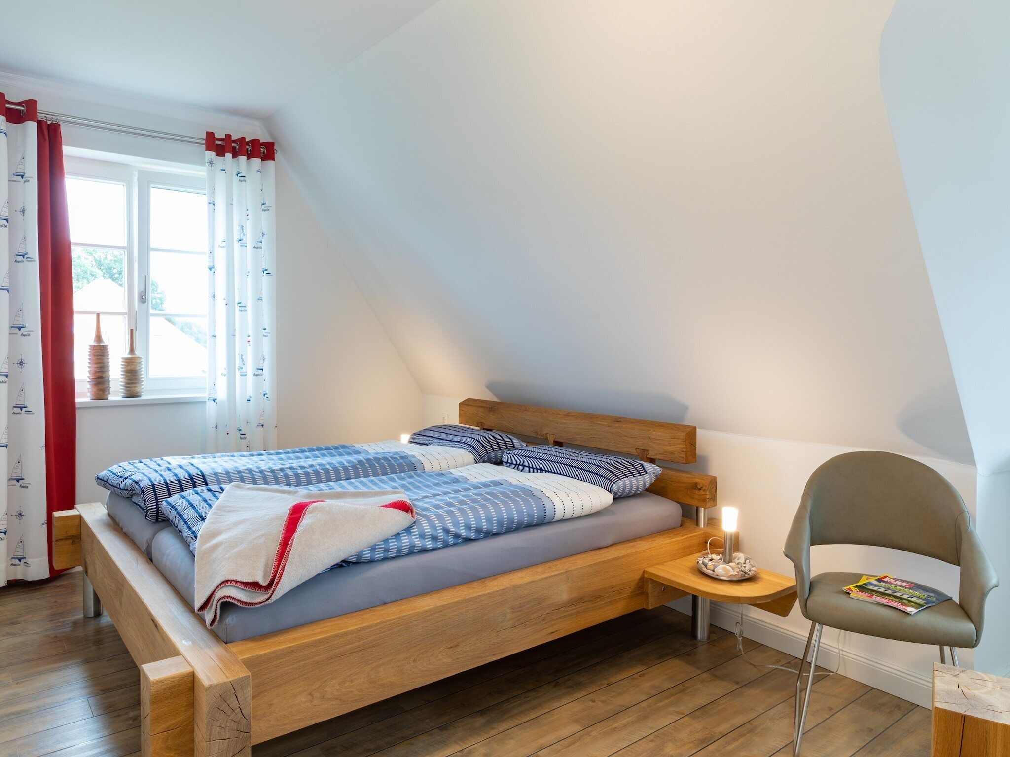 A bedroom with a wooden bed, a bedside table with a lamp, and a chair with a magazine.