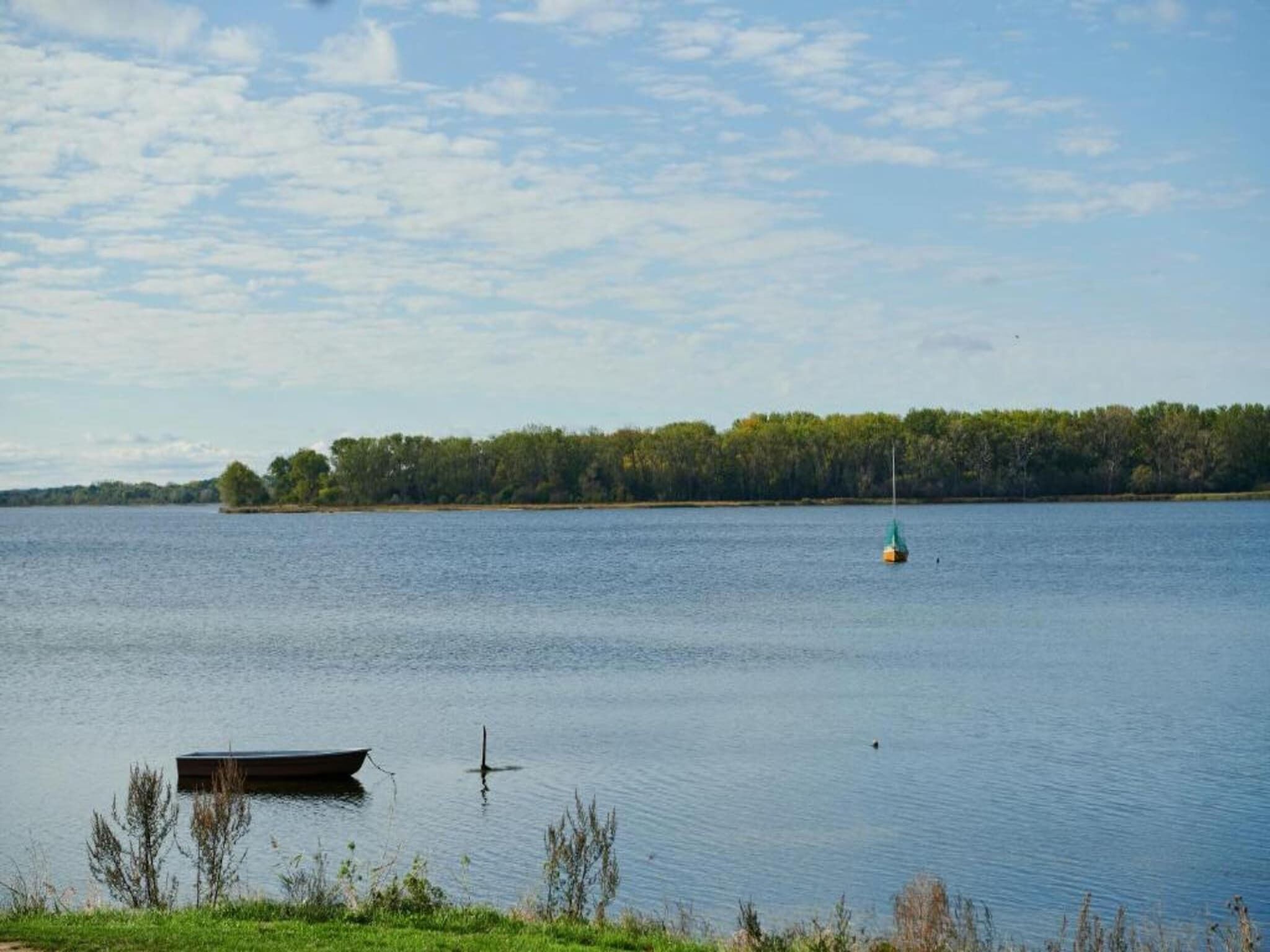 Um lago tranquilo com um pequeno barco atracado na margem e uma bóia flutuando na água.