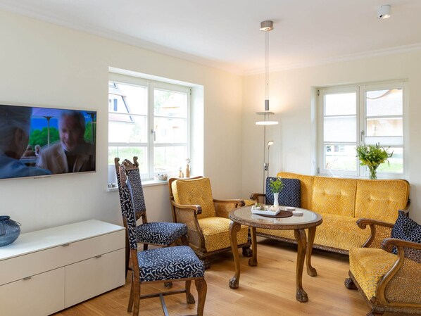 Un salon comprenant un canapé, deux fauteuils, une table basse et un téléviseur fixé au mur.