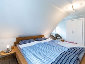 Une chambre avec un plafond en pente, un lit avec une literie à rayures, une table de chevet avec une lampe et une armoire.