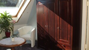 A room with a large wooden wardrobe, a white chair, a small round table with a lace tablecloth, and a potted plant. - Apartment in Bad Doberan mit Garten (Bad Doberan)
