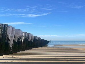 Une plage avec une longue et droite promenade en bois qui mène à l’eau.