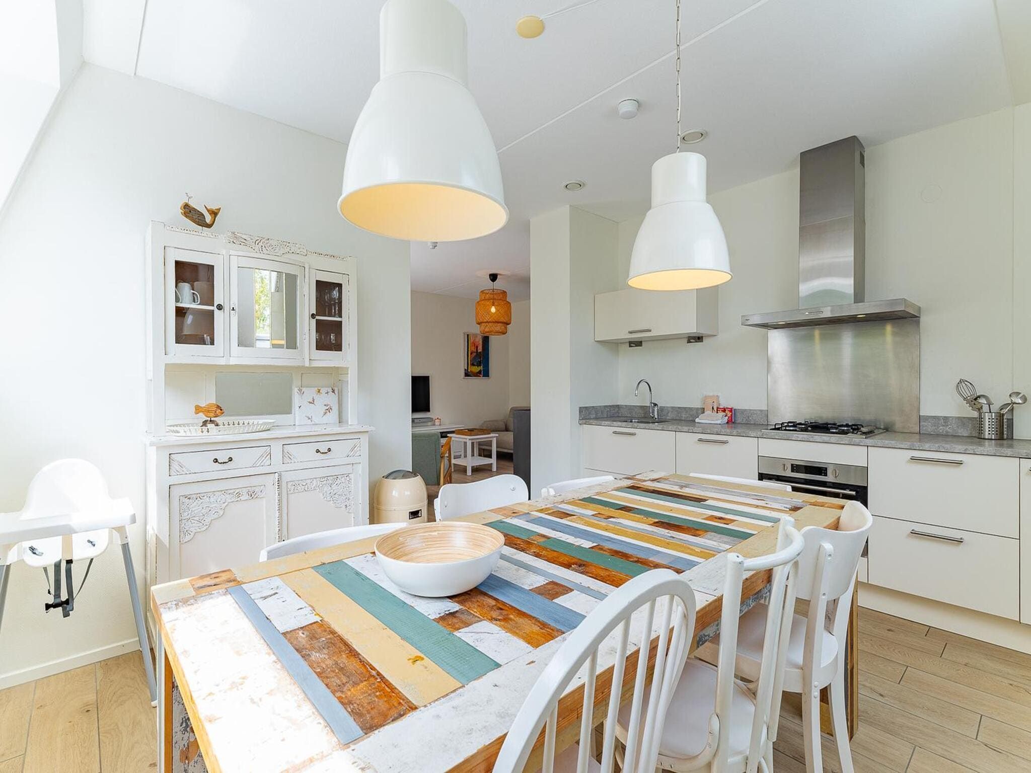 A modern kitchen with white cabinetry, a stainless steel range hood, and pendant lighting.
