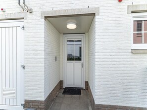 A white door with a glass panel, a small overhang, and a doormat at the entrance of a building with white brick walls.